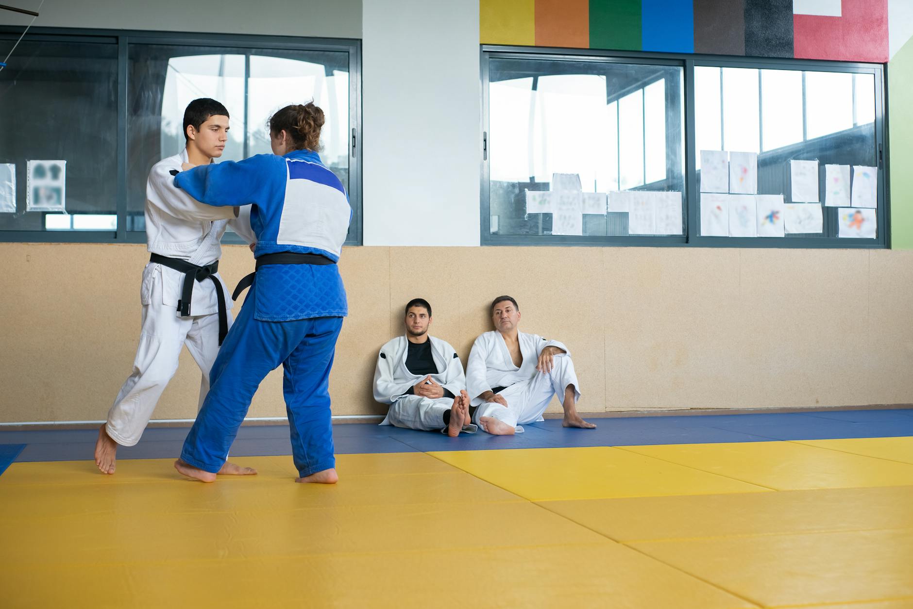 Kobieta i mężczyzna ćwiczą techniki judo na macie w dojo, inni obserwują