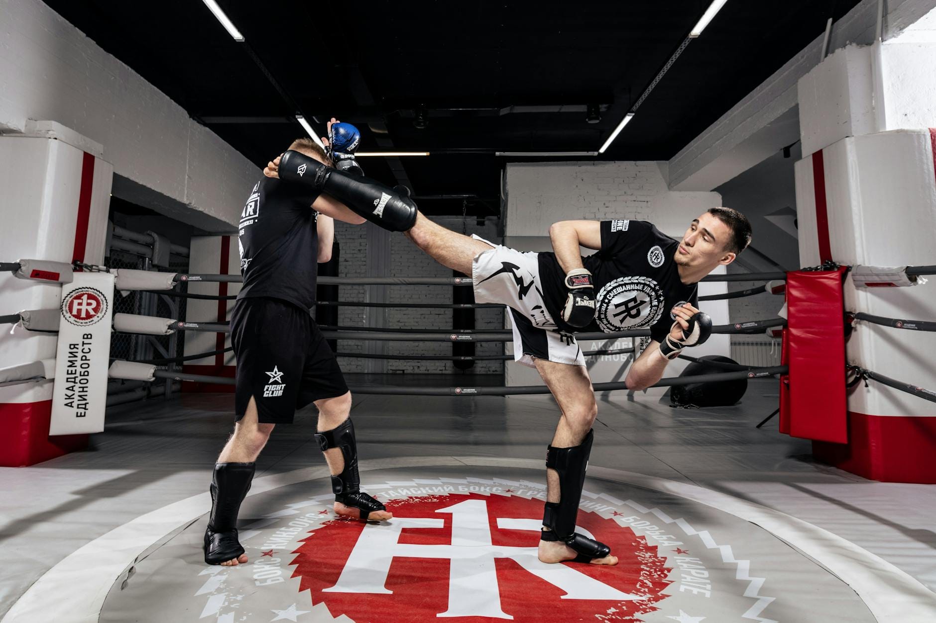Dwóch mężczyzn trenuje kickboxing w sali, ćwicząc obronę korpusu