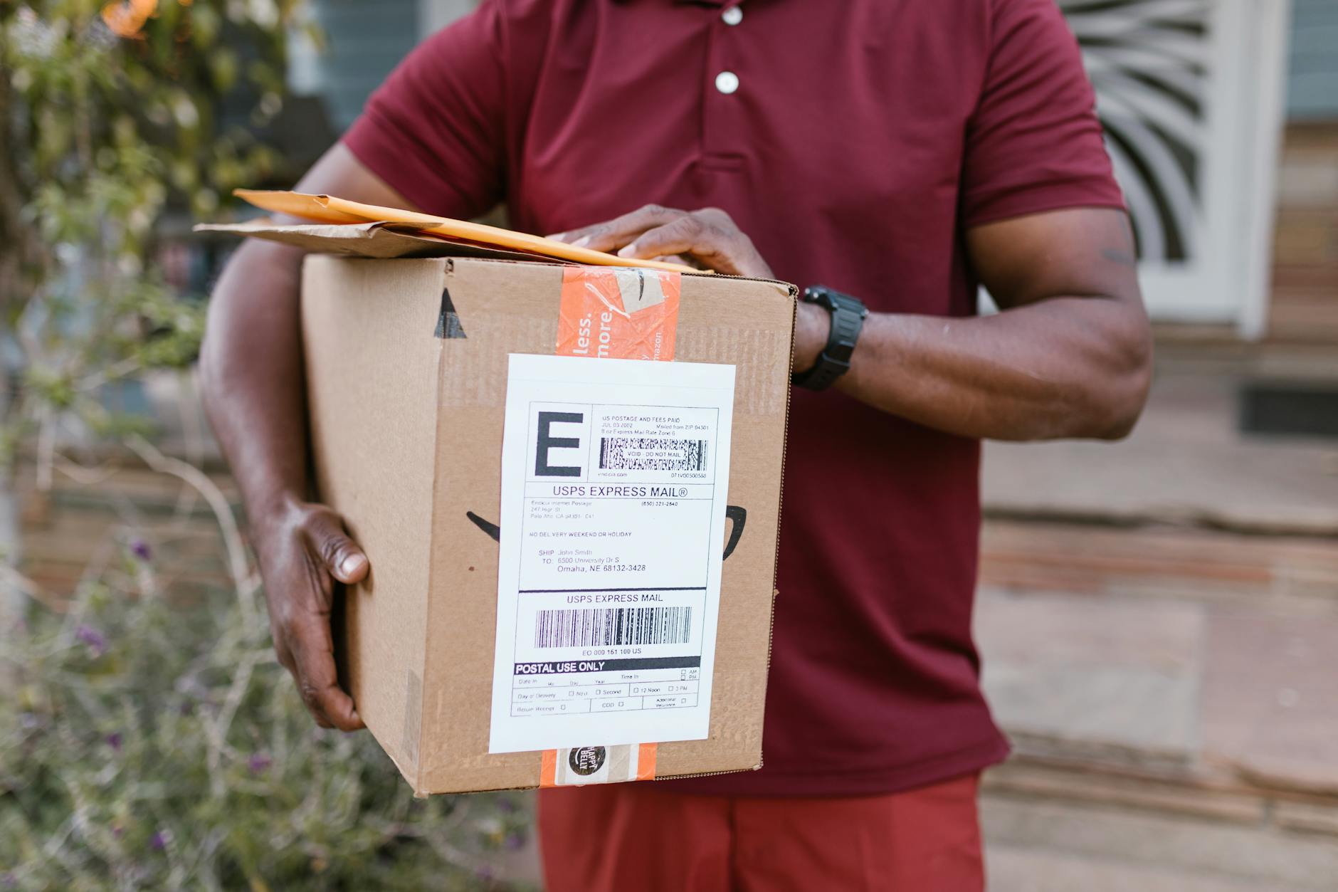 Kurier trzyma paczkę z etykietą USPS Express Mail przed domem