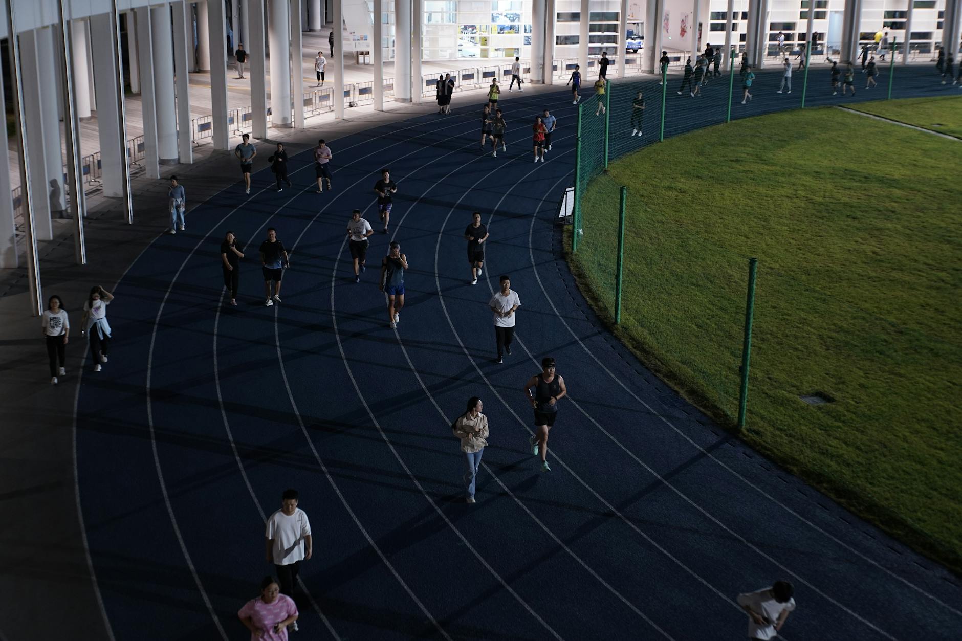 Grupa osób biegnąca wieczorem po miejskiej bieżni joggingowej Grupa osób biegnąca wieczorem po miejskiej bieżni joggingowej