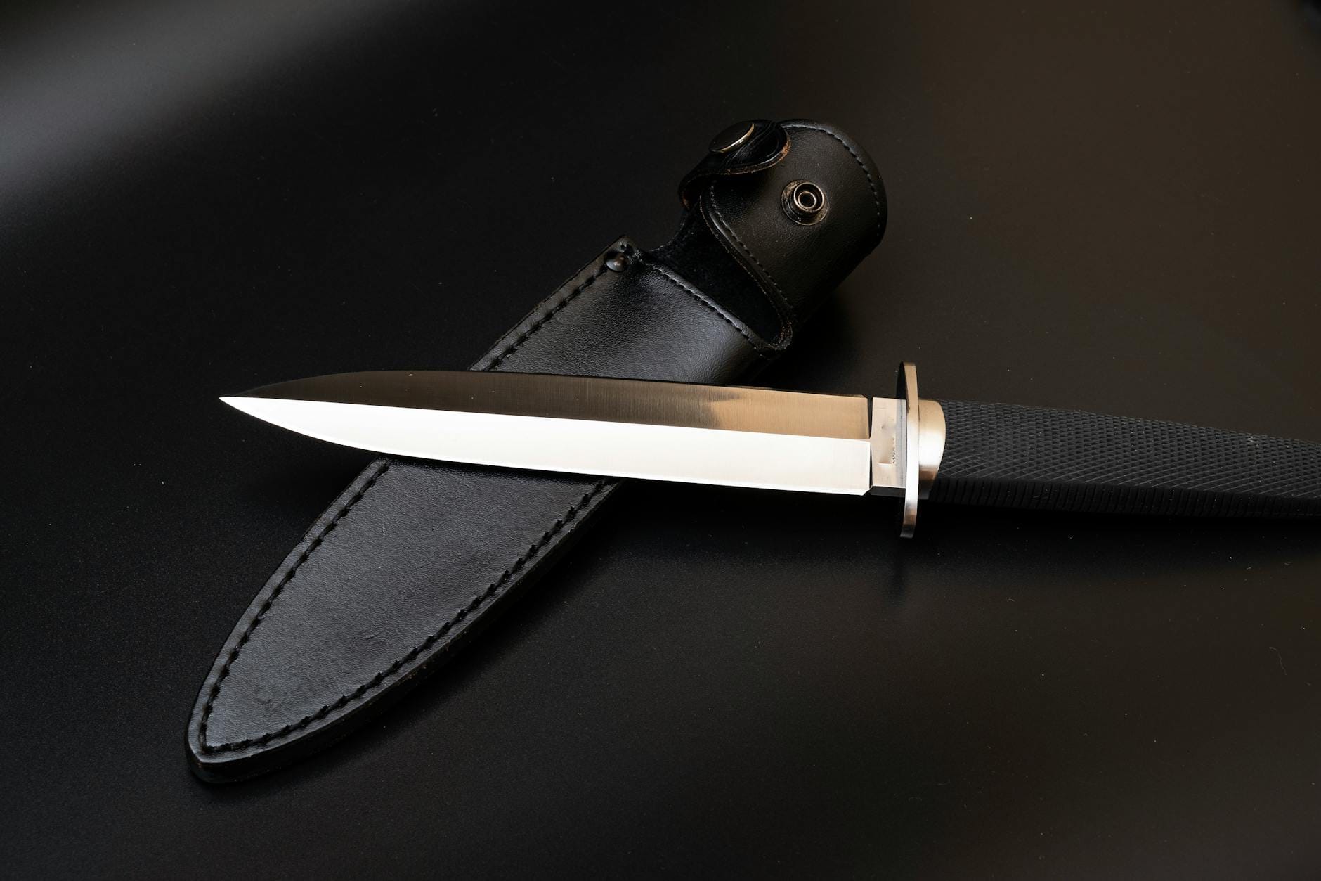 Nóż typu dagger ze skórzaną pochwą na ciemnym tle