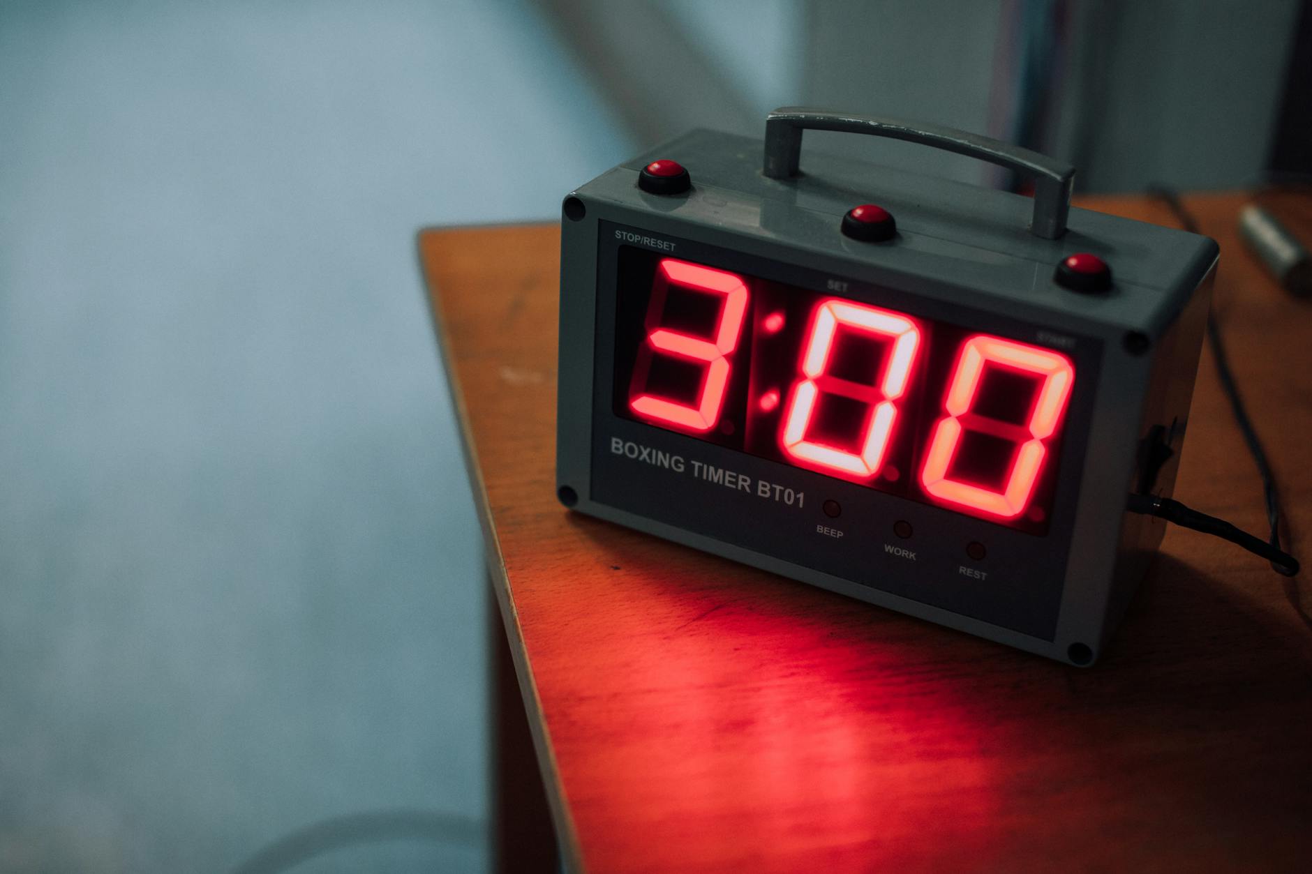 Trening ciosów prostych w domu: technika, oddech i tempo Bokserski timer ustawiony na 3 minuty leży na drewnianym stole