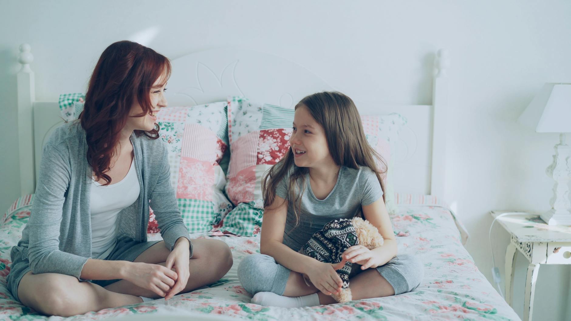 Jak uczyć dziecko mówić „nie” bez poczucia winy Mama i córka uśmiechają się, leżąc razem na łóżku w przytulnym pokoju