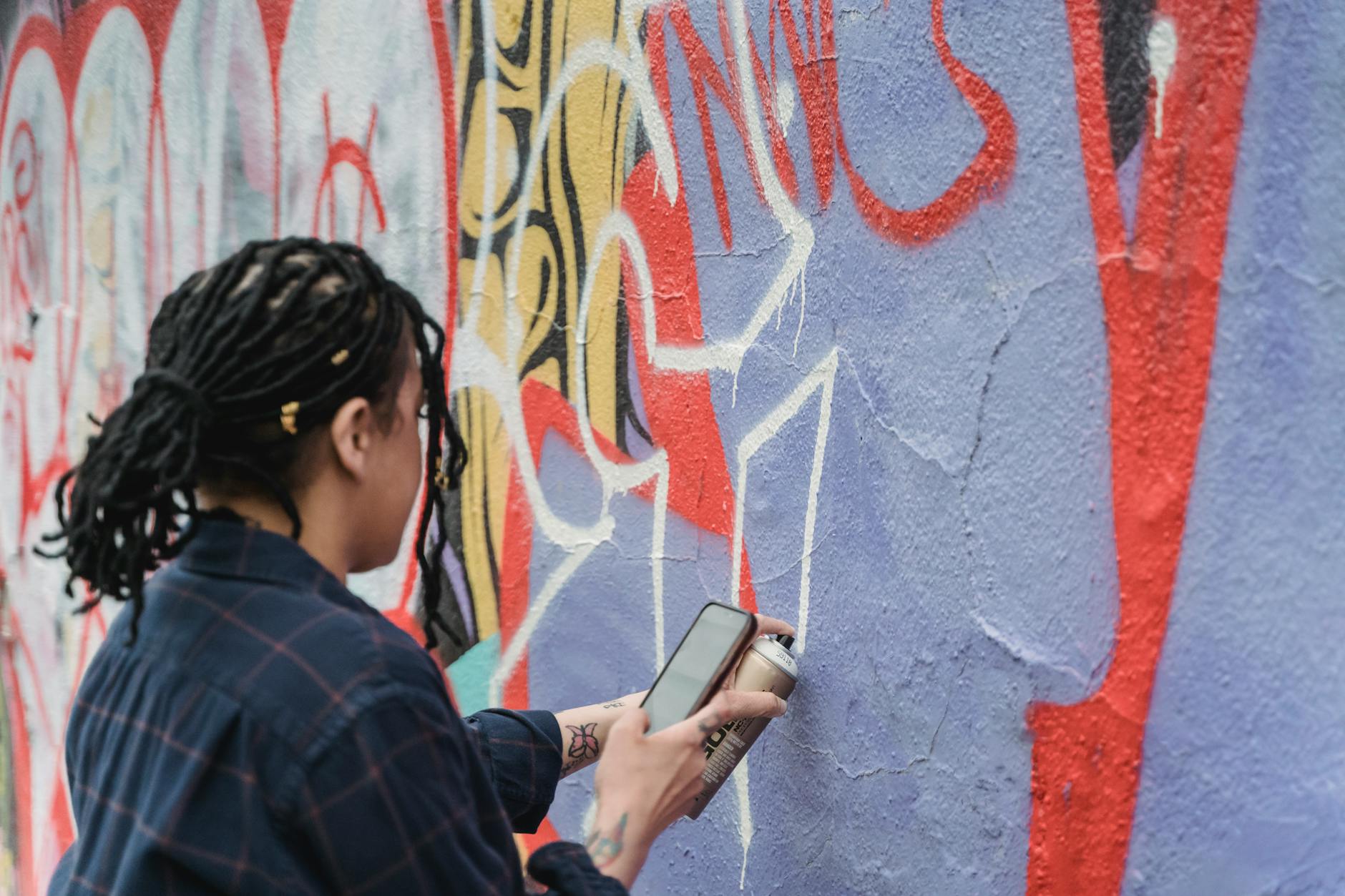 Osoba malująca kolorowe graffiti sprayem na zewnętrznej ścianie