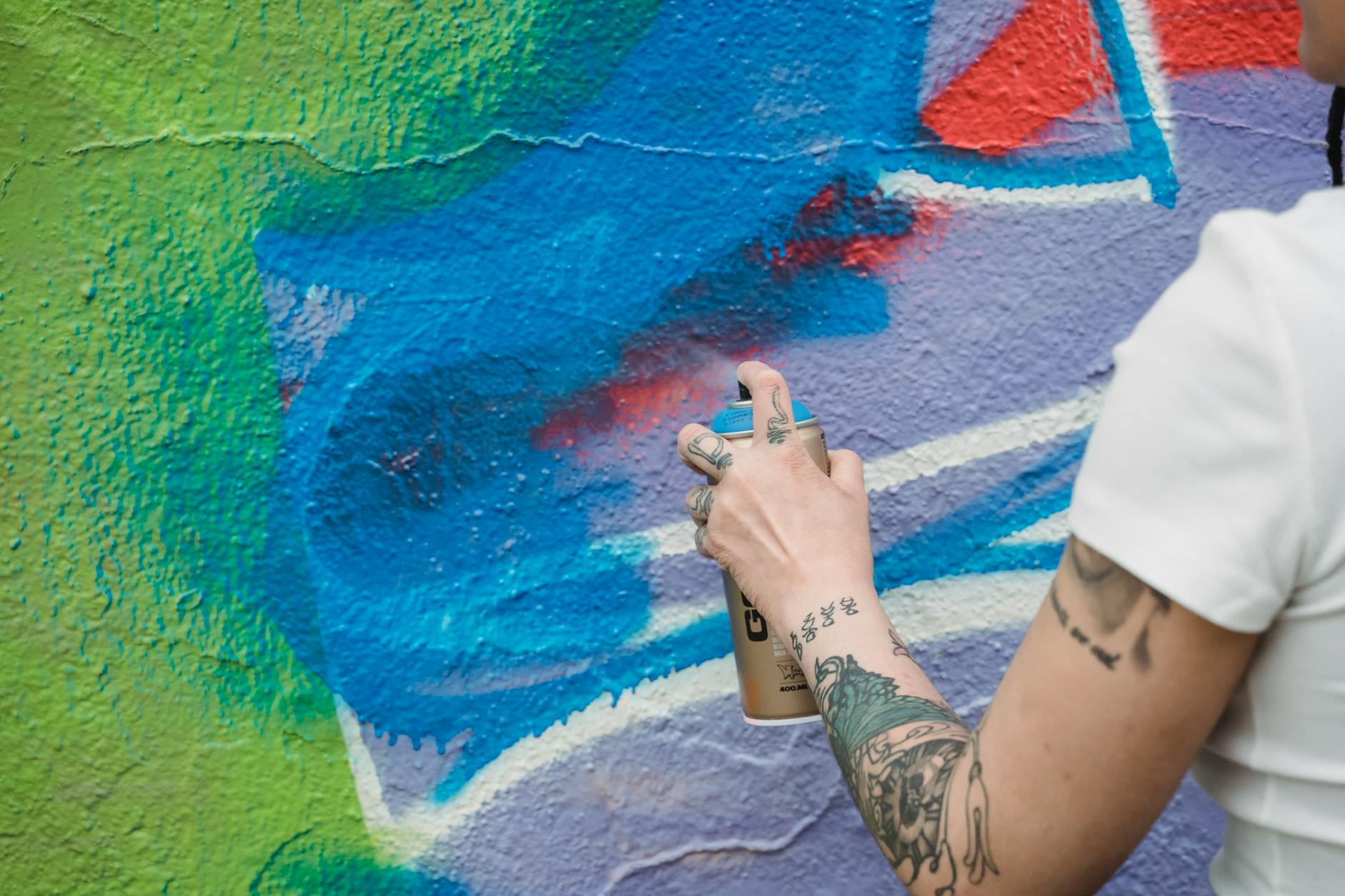 Wytatuowana dłoń malująca kolorowe graffiti sprayem na murze
