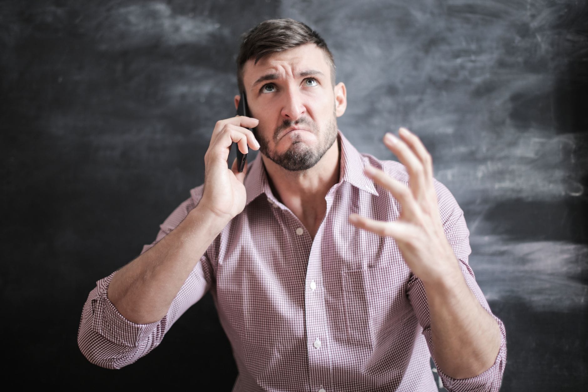 Zestresowany mężczyzna w różowej koszuli rozmawia przez telefon w pomieszczeniu